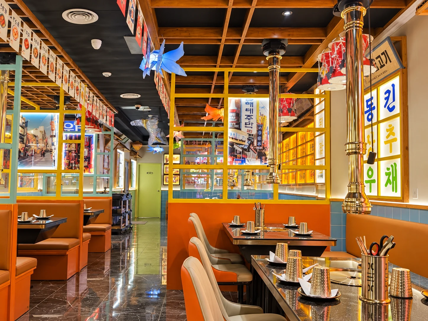 Sala de jantar do Incheon com bancos laranja, divisórias amarelas e grelhas nas mesas